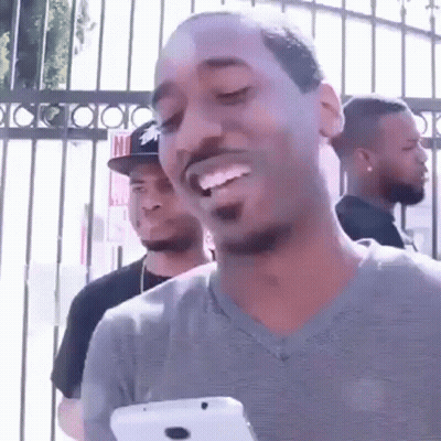 A Man Is Smiling While Holding A Cell Phone In Front Of A Fence . GIF