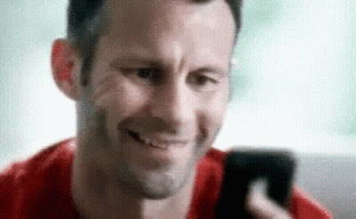 A Man Is Smiling While Looking At His Phone GIF