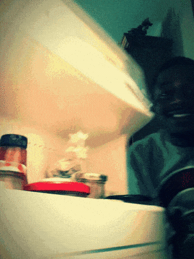 A Man Is Smiling While Looking Into A Refrigerator Filled With Jars Of Food GIF