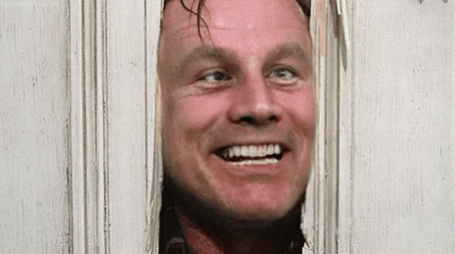 A Man Is Smiling While Looking Through A Door . GIF