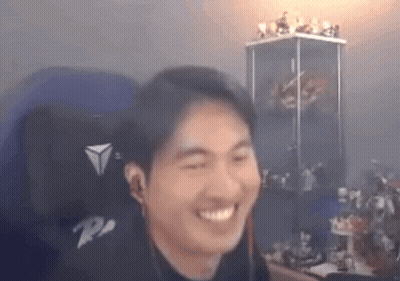 A Man Is Smiling While Sitting In A Chair In Front Of A Display Case Of Figurines . GIF