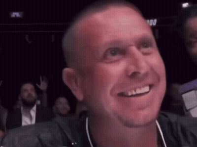 A Man Is Smiling While Sitting In A Crowd Of People . GIF