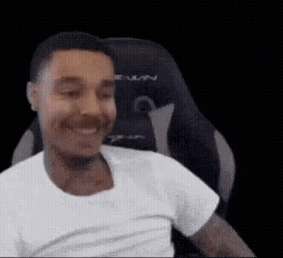 A Man Is Smiling While Sitting In A Gaming Chair . GIF