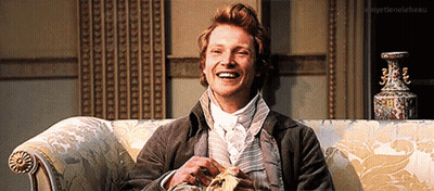 A Man Is Smiling While Sitting On A Couch With A Vase In The Background .. GIF