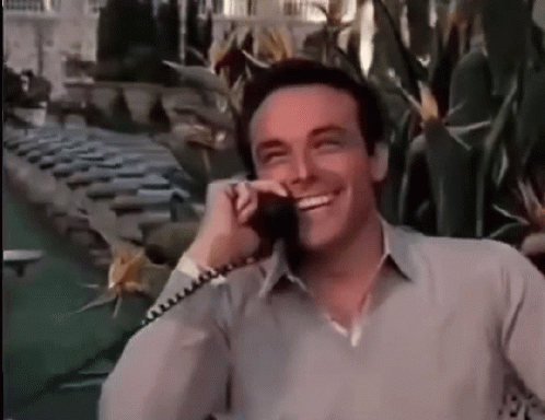 A Man Is Smiling While Talking On A Phone In Front Of A Pool . GIF