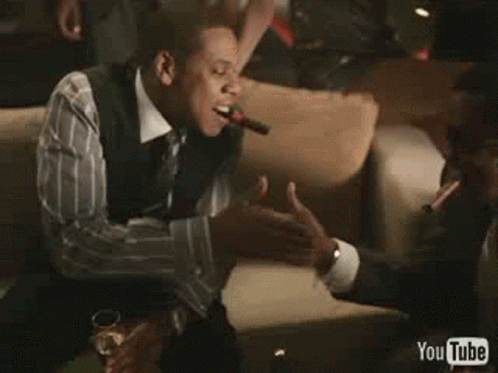 A Man Is Smoking A Cigar And Shaking Hands With Another Man In A Room . GIF