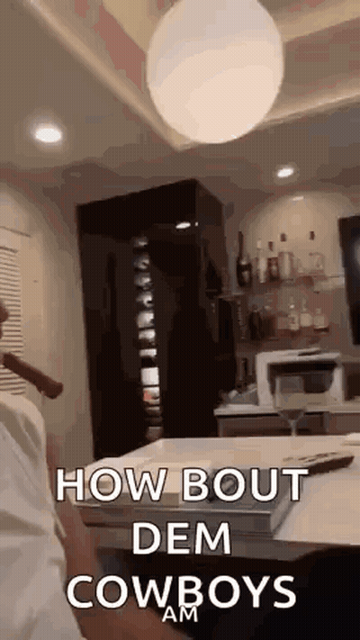A Man Is Smoking A Cigar In A Living Room With The Words `` How Bout Dem Cowboys Am '' Written On It . GIF