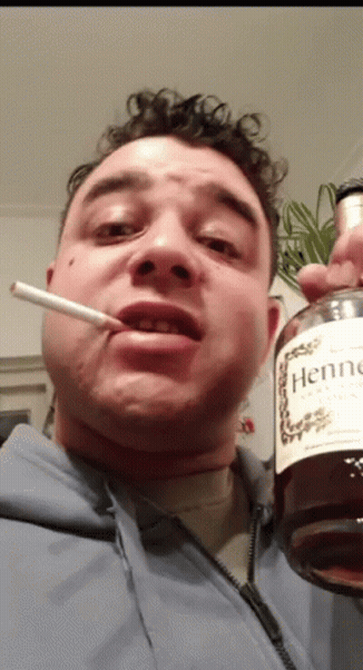 A Man Is Smoking A Cigarette And Holding A Bottle Of Hennessy Cognac GIF