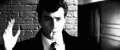 A Man Is Smoking A Cigarette In Front Of A Brick Wall . GIF