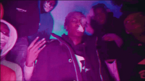 A Man Is Smoking A Cigarette In Front Of A Group Of People In A Purple Light . GIF