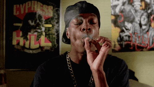A Man Is Smoking A Cigarette In Front Of A Poster That Says Cypress Hill GIF