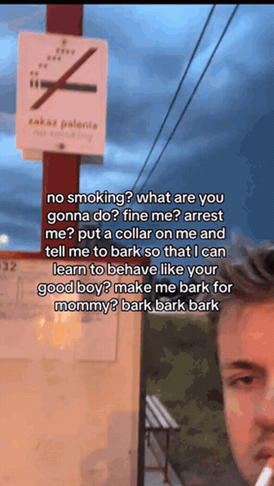 A Man Is Smoking A Cigarette In Front Of A Sign That Says No Smoking GIF