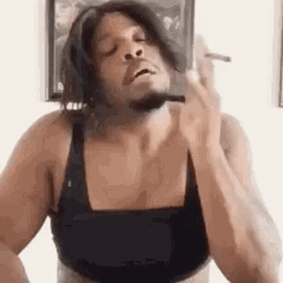 A Man Is Smoking A Cigarette While Wearing A Bra . GIF