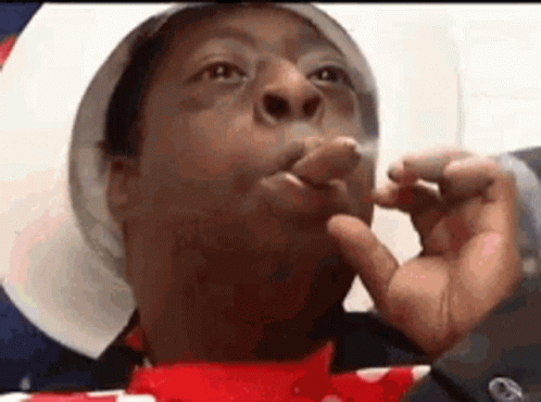A Man Is Smoking A Cigarette With His Fingers In His Mouth . GIF
