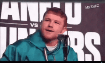 A Man Is Speaking Into A Microphone In Front Of A Sign That Says Alvarez GIF
