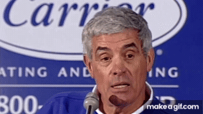 A Man Is Speaking Into A Microphone In Front Of A Sign That Says Carrier GIF