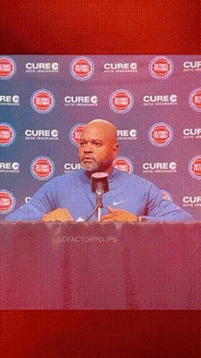 A Man Is Speaking Into A Microphone In Front Of A Wall That Says Cure GIF