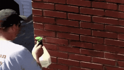 A Man Is Spraying A Brick Wall With A Sprayer GIF