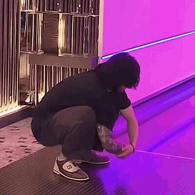 A Man Is Squatting Down In Front Of A Bowling Alley With Purple Lights . GIF