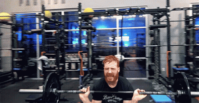 A Man Is Squatting With A Barbell In A Gym Wearing A Shirt That Says Bear Earring GIF