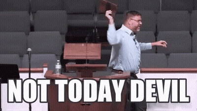 A Man Is Standing At A Podium With The Words Not Today Devil Written On The Wall Behind Him . GIF