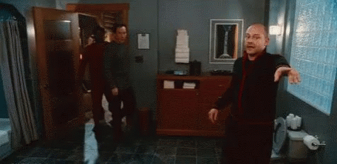 A Man Is Standing In A Bathroom With Another Man . GIF