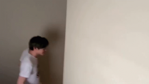 A Man Is Standing In A Corner Of A Room . GIF