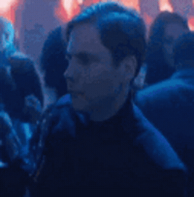 A Man Is Standing In A Crowd Of People At A Party And Looking At The Camera . GIF