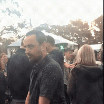 A Man Is Standing In A Crowd Of People With A Green Light In The Background GIF