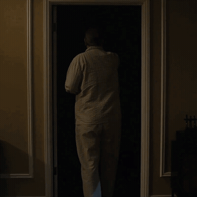 A Man Is Standing In A Dark Closet With A Lamp On GIF