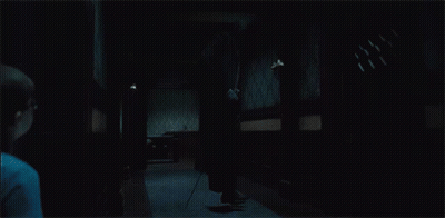 A Man Is Standing In A Dark Hallway Holding A Cane GIF