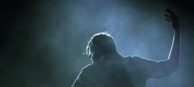 A Man Is Standing In A Dark Room With His Arms Outstretched In The Air . GIF