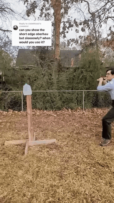 A Man Is Standing In A Field Holding A Hammer And A Bottle Of Water . GIF