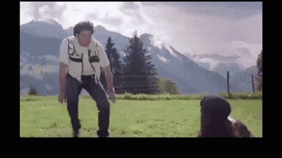 A Man Is Standing In A Field With Mountains In The Background While A Woman Looks On GIF