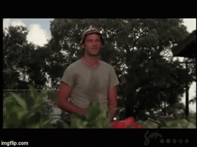 A Man Is Standing In A Garden With A Lawn Mower In His Hand . GIF