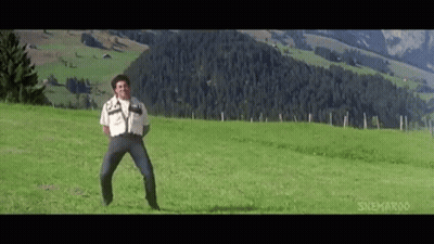 A Man Is Standing In A Grassy Field In Front Of A Mountain . GIF