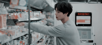 A Man Is Standing In A Grocery Store Reaching For A Bottle Of Water . GIF