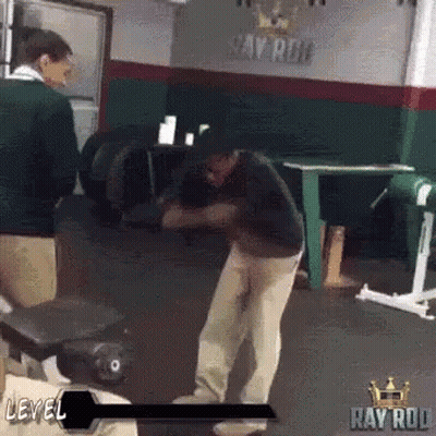 A Man Is Standing In A Gym In Front Of A Sign That Says Ray Rod . GIF