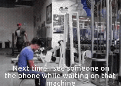 A Man Is Standing In A Gym Looking At His Phone GIF