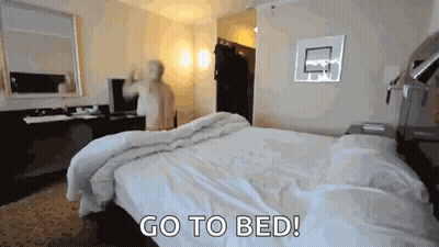 a man is standing in a hotel room with the words go to bed behind him