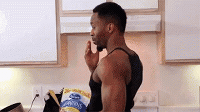 A Man Is Standing In A Kitchen With A Bag Of Raisins In His Hand . GIF