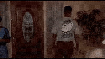 A Man Is Standing In A Living Room Wearing A T-Shirt With A Picture Of Santa Claus On The Back . GIF