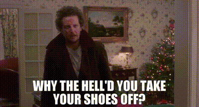 A Man Is Standing In A Living Room With A Christmas Tree In The Background And A Picture On The Wall . GIF