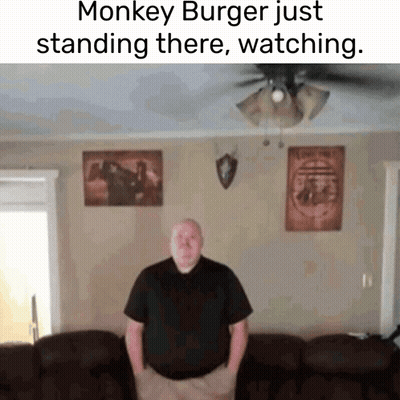 A Man Is Standing In A Living Room With A Monkey Burger Just Standing There Watching GIF