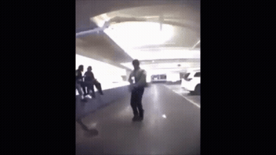 A Man Is Standing In A Parking Garage With A Group Of People Sitting On A Bench . GIF