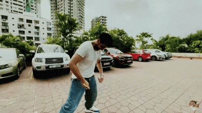 A Man Is Standing In A Parking Lot With A Ford Car Parked Behind Him GIF