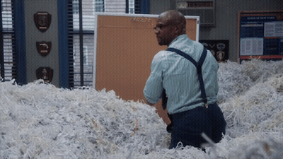 A Man Is Standing In A Pile Of Shredded Paper In Front Of A Bulletin Board That Says News Of New York GIF