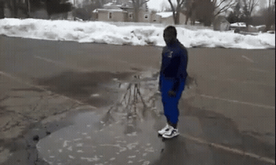 A Man Is Standing In A Puddle Of Water On The Side Of A Road . GIF