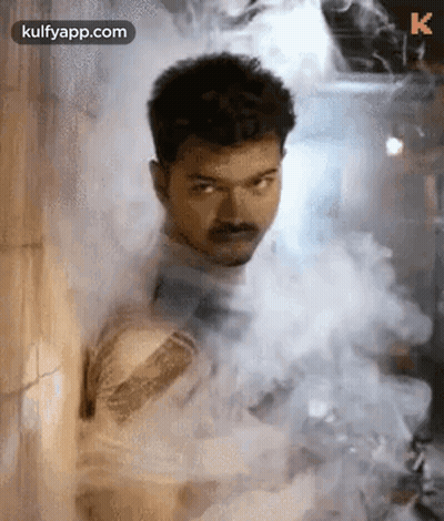 A Man Is Standing In A Room Covered In Smoke . GIF
