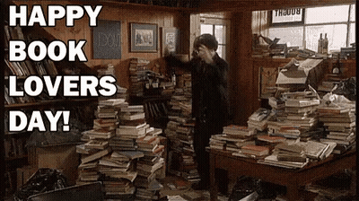 A Man Is Standing In A Room Filled With Lots Of Books And A Sign That Says Happy Book Lovers Day . GIF